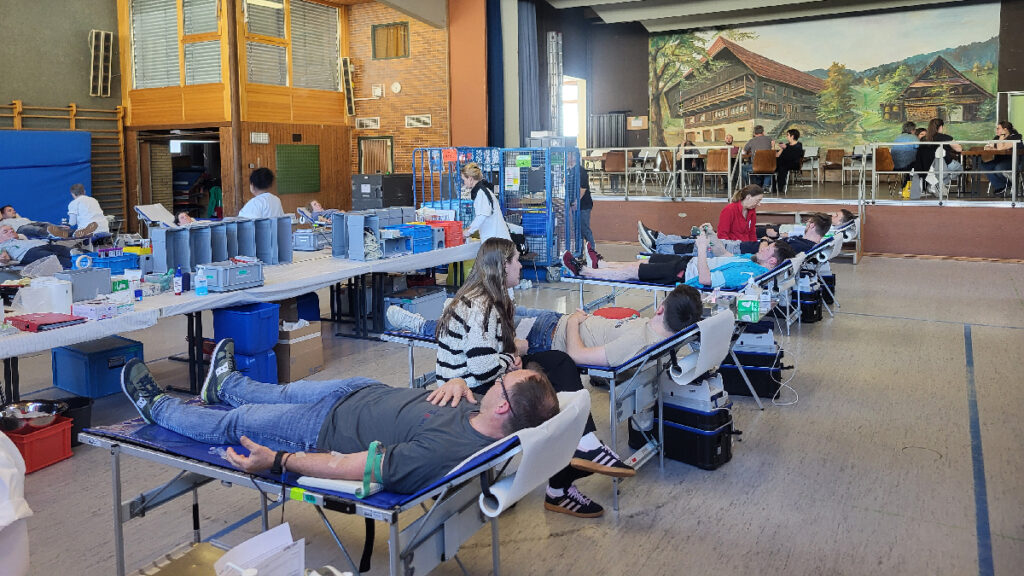 Das Bild zeigt die Turn- und Festhalle Steinach, in der gerade die Blutspendeaktion stattfindet. Zu sehen ist das Blutspendeteam und einige Spenderinnen und Spender.