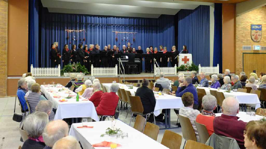 Das Foto zeigt die Bühne der Steinacher Turn- und Festhalle, auf der der Gesangverein "Unser Chor" zu sehen ist. Im Publikum sitzen Senioren.