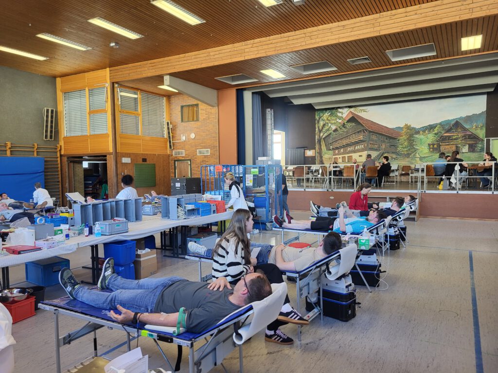 Das Bild zeigt die Turn- und Festhalle Steinach, in der gerade die Blutspendeaktion stattfindet. Zu sehen ist das Blutspendeteam und einige Spenderinnen und Spender.